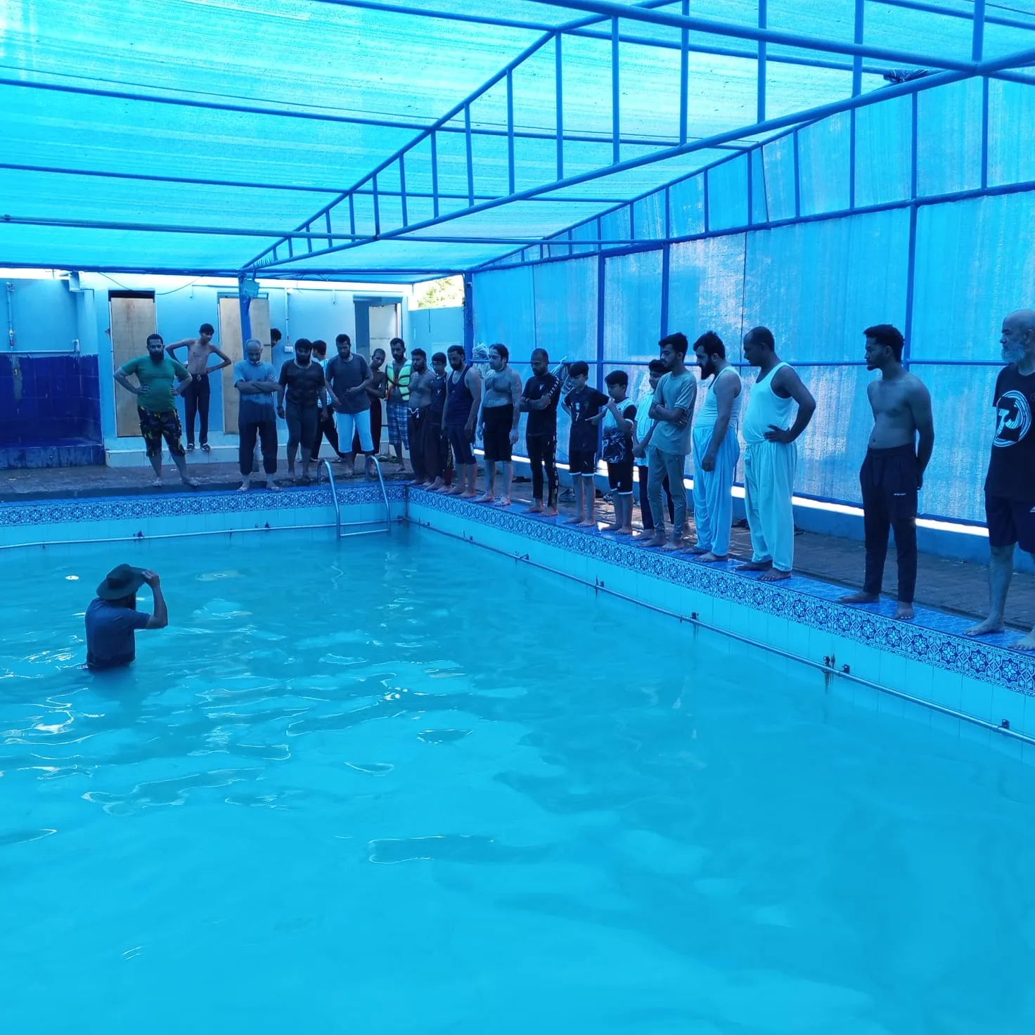 Students watching Zeeshan demonstrate a swimming skill in the pool.